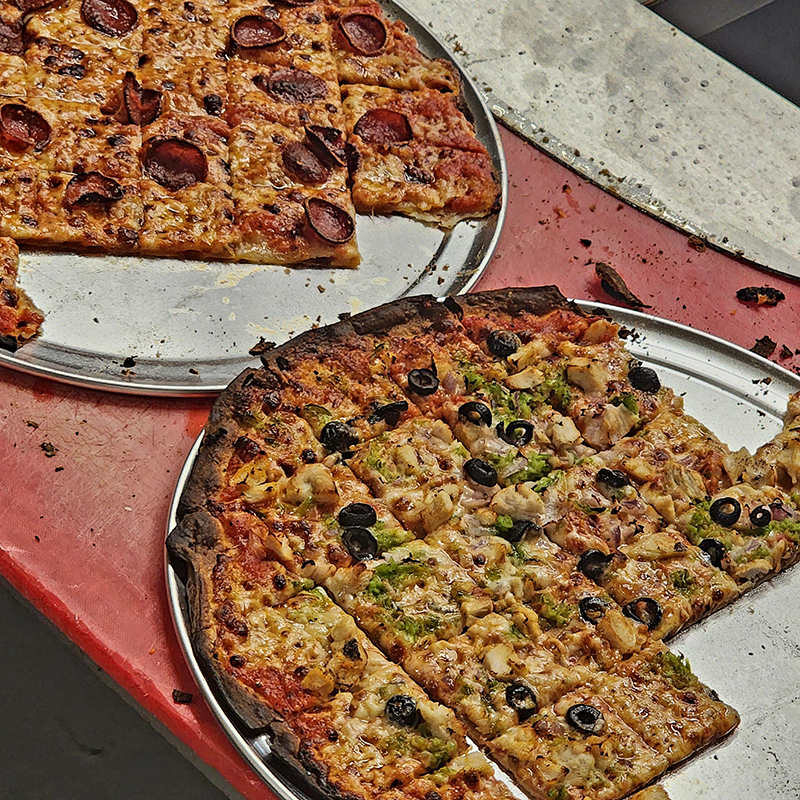 a photo of two fresh pizzas stacked with toppings. several square slices are missing from each.
